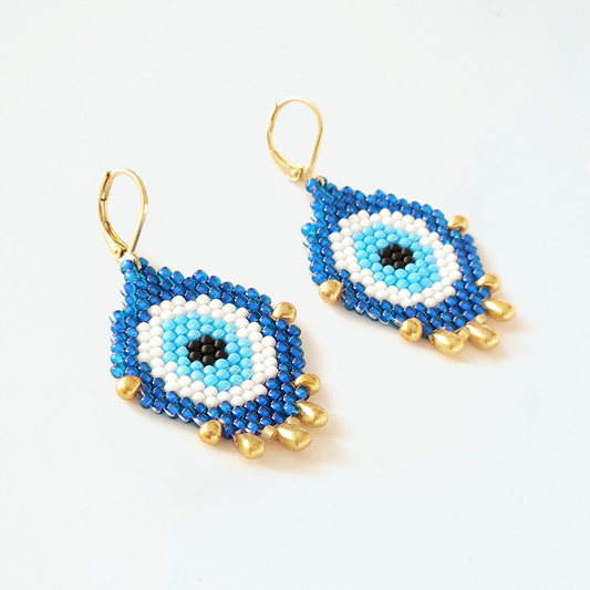 Pair of evil eye beaded earrings with blue, white, and gold colors on a light gray background