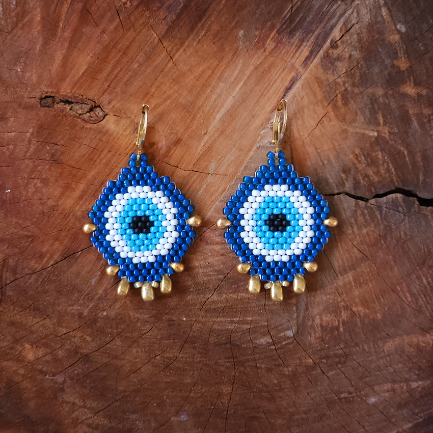 Pair of blue and white evil eye beaded earrings on a wooden surface