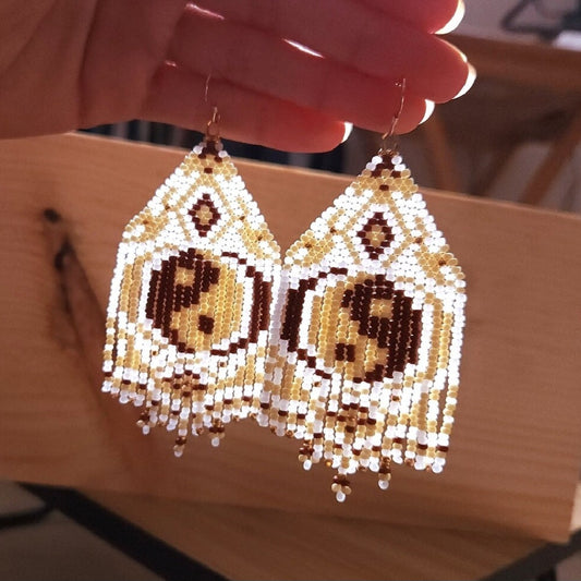Beaded earrings with intricate patterns held by a hand on a wooden surface.