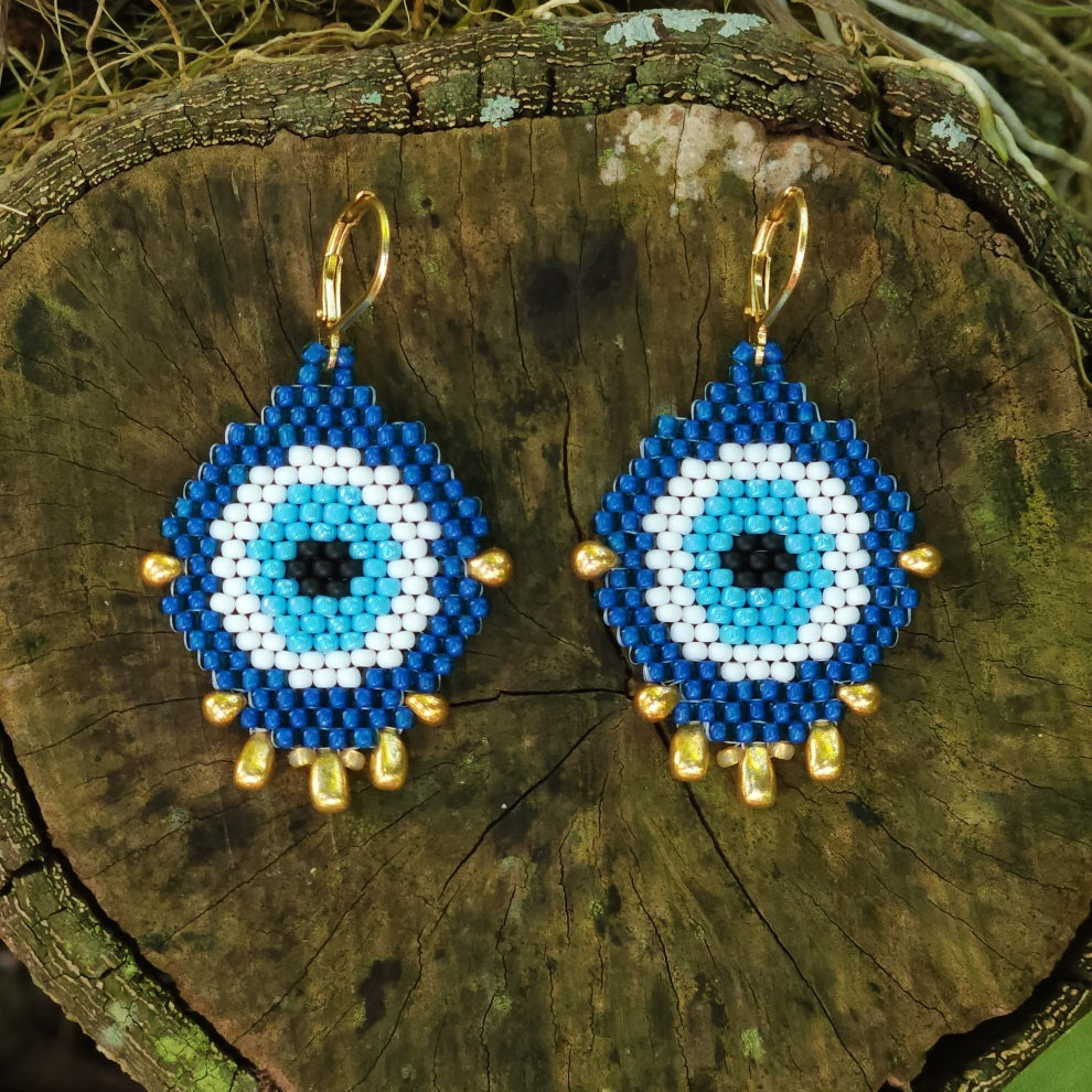 Blue and white evil eye beaded earrings with gold accents on a wooden surface