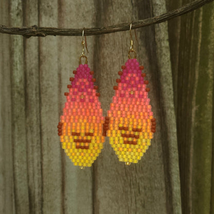 Pixelated fire design earrings hanging on a branch with a wooden background