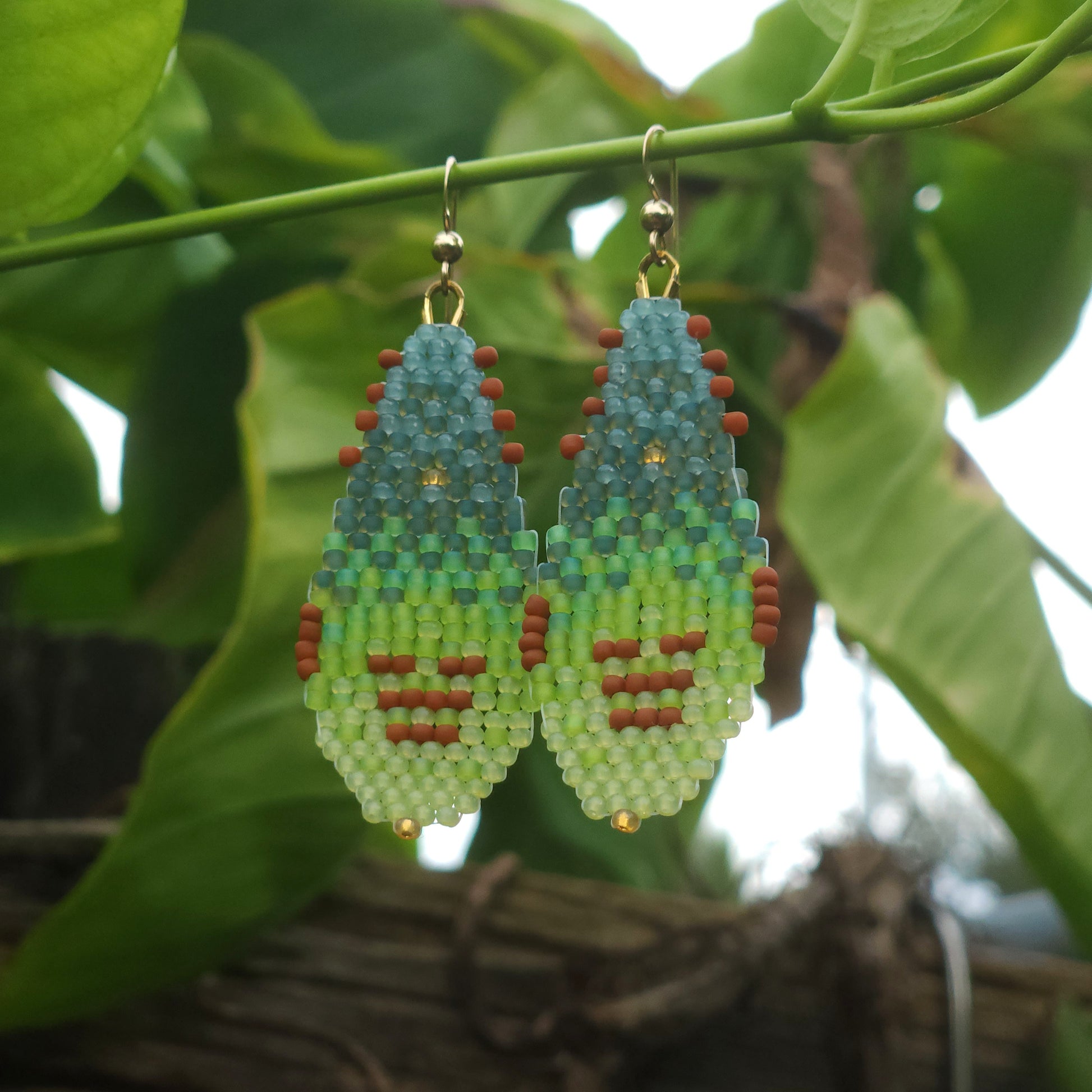 Pair of beaded earrings hanging on a branch with green leaves in the background